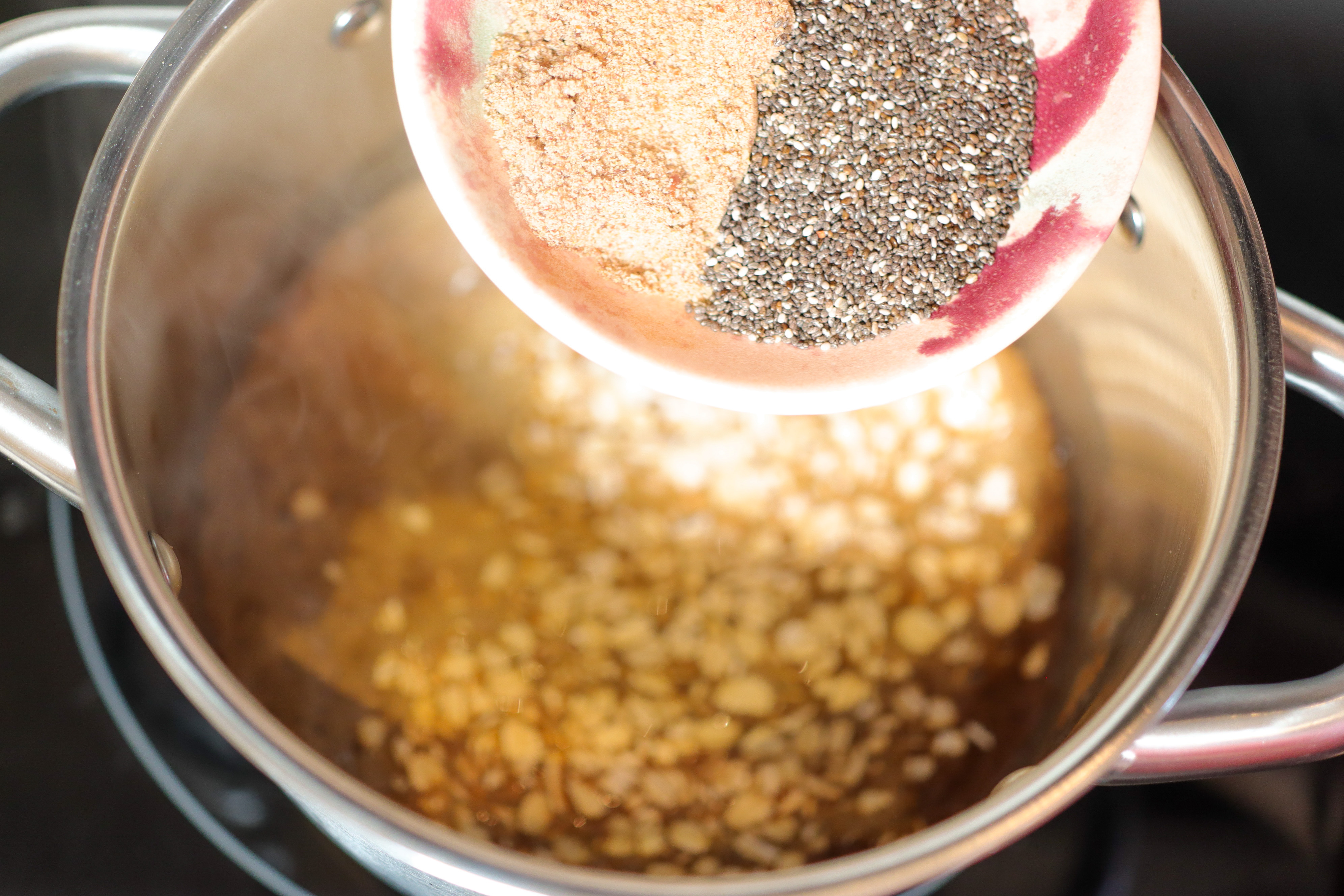 a bowl of seeds being poured into a pot of oatmeal