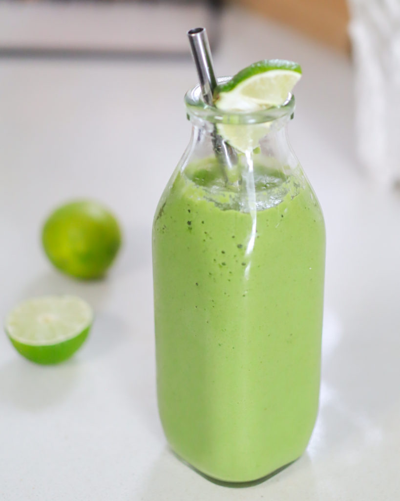 Glass jar with green smoothie inside with a sliced lime in the background