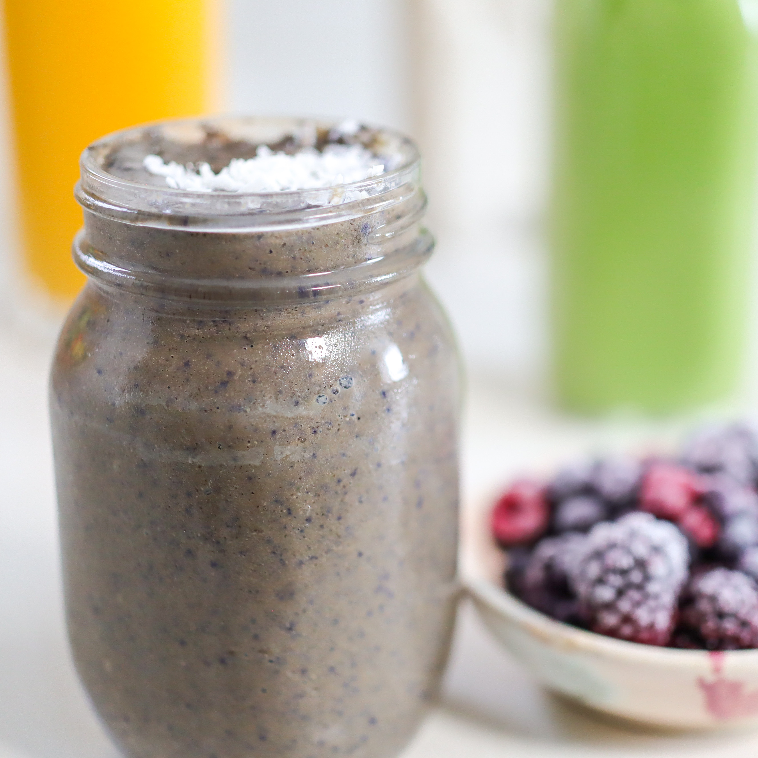 smoothie in a jar next to bowl of frozen berries