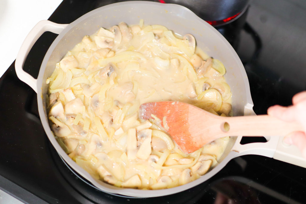 Hand stirring pasta in a saucepan.