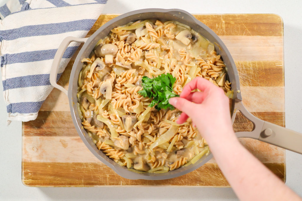 Hand placing fresh parsley in a saucepan of pasta.