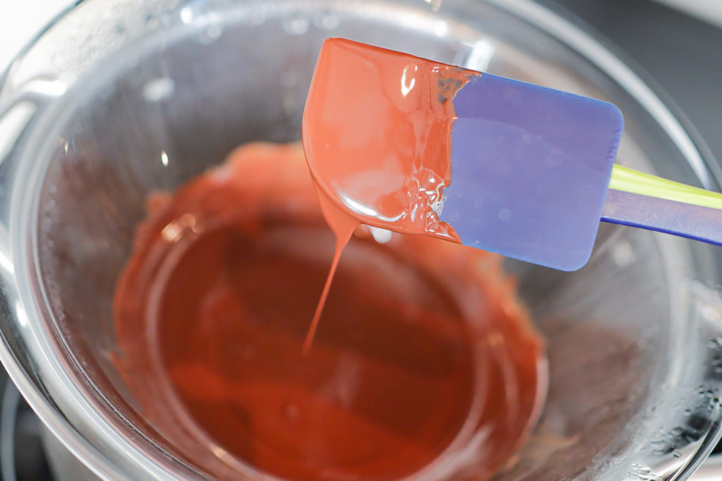 Melted chocolate dripping off a spatula over a bowl.