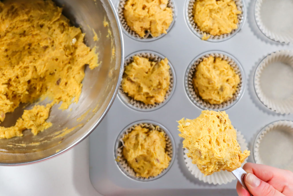 Hand scooping batter into a muffin tin.