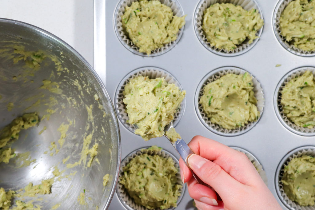 Hand pouring batter into a muffin tin.