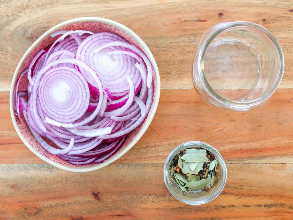 a bowl of sliced rd onions, a small jar of spices, a large empty jar