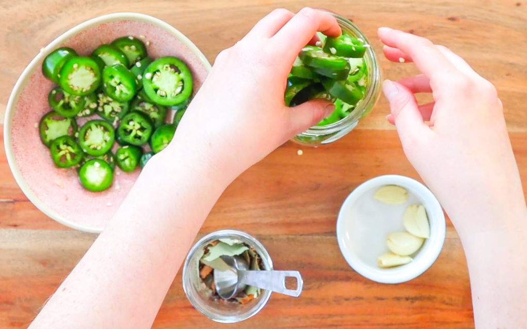 hands placing sliced jalapenos into a jar