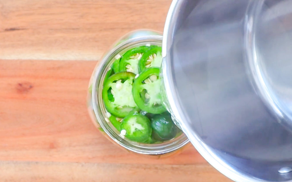 pouring hot liquid into jar of jalapeños